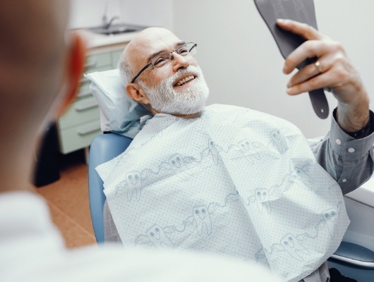 Senior dental patient admiring his new smile in mirror