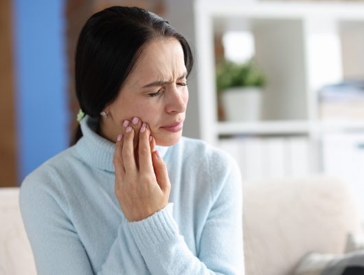 Woman in light blue sweater holding her cheek in pain