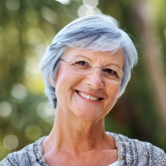 Senior woman smiling with implant dentures in Denton