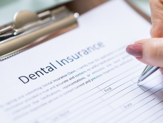 Close up of person filling out paperwork for dental insurance in Denton