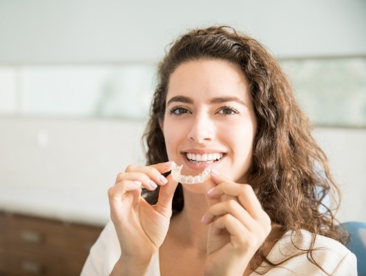 Woman with curly brown hair holding Invisalign tray