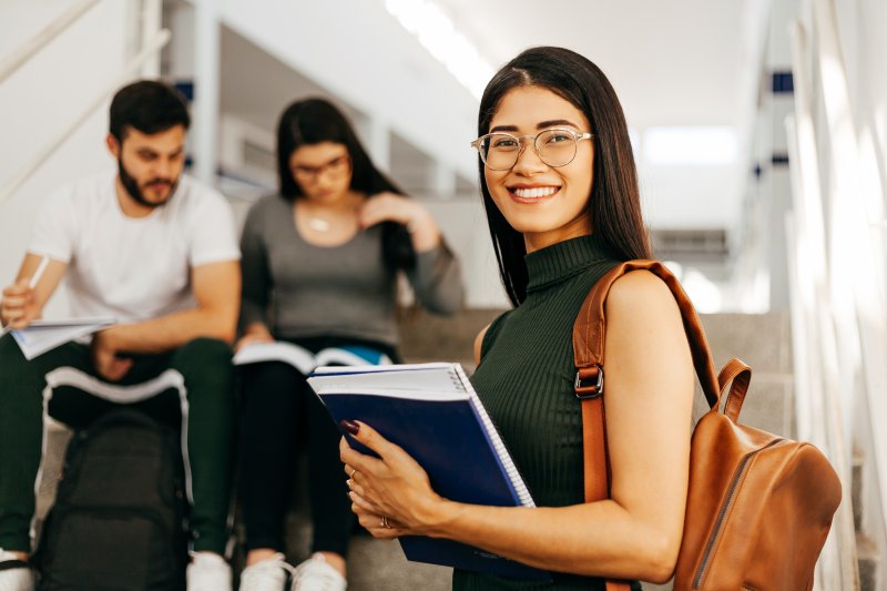 A smiling student carrying books in a college setting